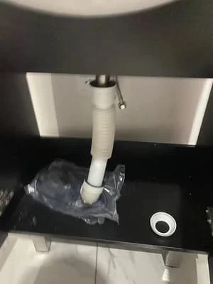 White PVC drain pipe and P-trap assembly installed under bathroom sink with black countertop