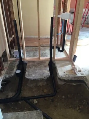 Excavated sewer line pit showing damaged underground pipes and foundation exposure