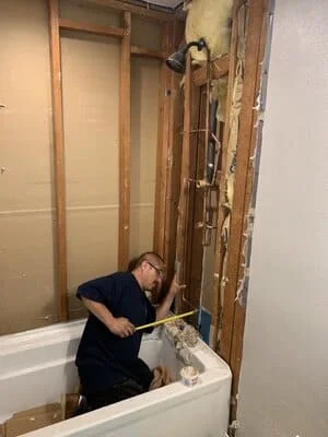 Plumber installing copper supply lines and PVC drain pipes in bathroom wall framing during rough-in phase
