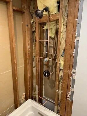 Bathroom plumbing rough-in with copper supply lines and drain pipes installed in wall framing