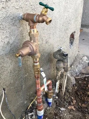 Brass outdoor faucet with dual valves and copper supply lines on concrete wall