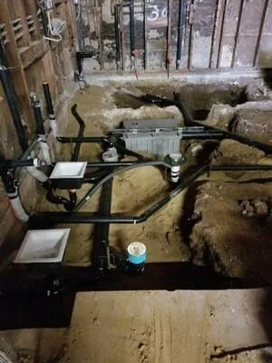 Sump pump installation with basin, check valves, and discharge piping in basement foundation