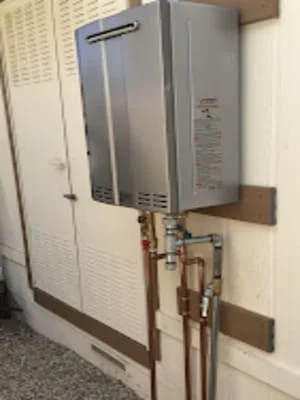 Stainless steel tankless water heater mounted on wall with copper piping connections