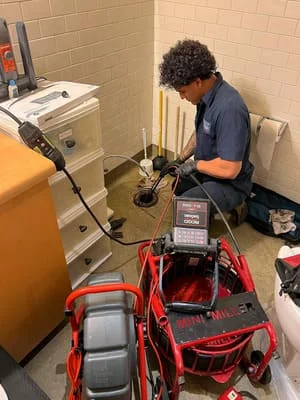 Plumber installing sump pump system with red basin and discharge piping in basement