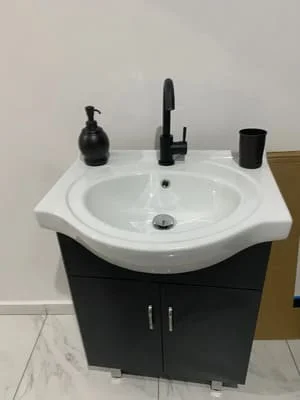 White porcelain sink with black matte faucet installed on black cabinet vanity with tile flooring