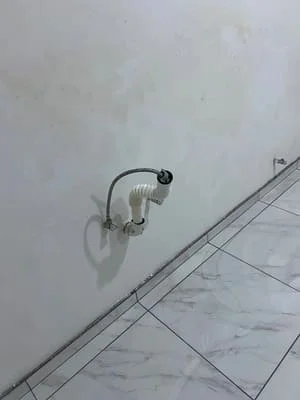 Chrome wall-mounted faucet with curved spout installed on marble tile backsplash with visible supply lines