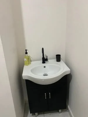 White curved sink with chrome faucet installed above black vanity cabinet in bathroom corner