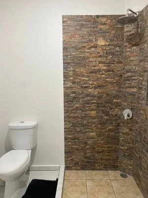 Bathroom with stacked stone tile shower surround, white toilet, and tile flooring